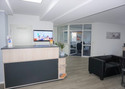 Empfangstresen und Sitzgruppe im Büro von Thomalla & Fischer Immobilien mit Bildschirm an der Wand