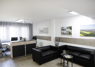 Empfangsbereich im Büro von Thomalla & Fischer Immobilien mit Ledersofas, Tresen und Bildern von Landschaften an der Wand
